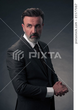 Portrait of a stylish elegant senior businessman with a beard and casual business clothes in photo studio isolated on dark background gesturing with hands Portrait of a stylish elegant senior businessman with a beard and casual business clothes in photo studio isolated on dark background gesturing with hands 85577087