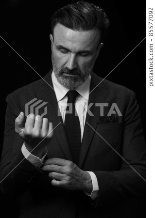 Portrait of a stylish elegant senior businessman with a beard and casual business clothes in photo studio adjusting suit 85577092