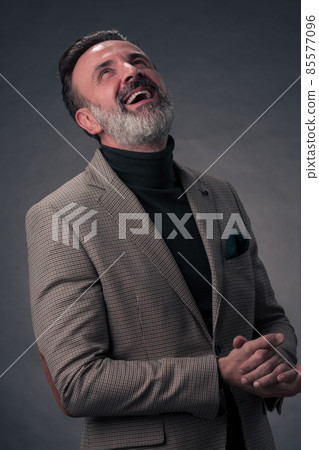 Portrait of a stylish elegant senior businessman with a beard and casual business clothes in photo studio isolated on dark background gesturing with hands Portrait of a stylish elegant senior businessman with a beard and casual business clothes in photo studio isolated on dark background gesturing with hands 85577096