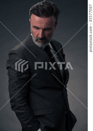 Portrait of a stylish elegant senior businessman with a beard and casual business clothes in photo studio isolated on dark background gesturing with hands Portrait of a stylish elegant senior businessman with a beard and casual business clothes in photo studio isolated on dark background gesturing with hands 85577097