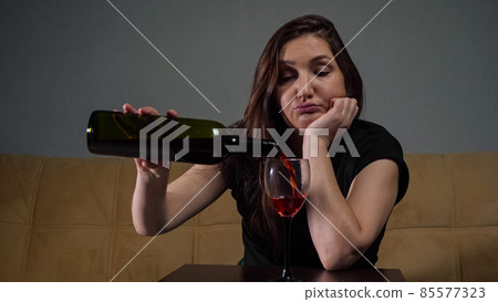 Woman pours wine into glass sitting stressed and depressed 85577323