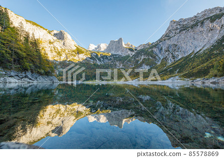 Beautiful view of idyllic colorful autumn scenery with Dachstein mountain summit reflecting in crystal clear Gosausee mountain lake in fall, Salzkammergut region, Upper Austria. Beautiful view of idyllic colorful autumn scenery with Dachstein mountain summit reflecting in crystal clear Gosausee mountain lake in fall, Salzkammergut region, Upper Austria. 85578869