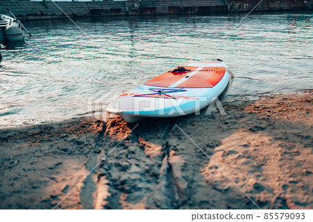 Close up of stand up SUP paddle board on lake or sea with blue water lilies, paddling in summer time at sunset. Summer family vacation Close up of stand up SUP paddle board on lake or sea with blue water lilies, paddling in summer time at sunset. Summer family vacation 85579093