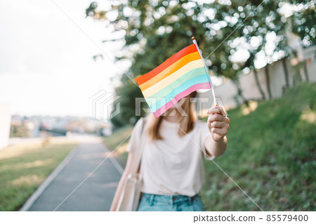 Beautiful caucasian lesbian woman holding rainbow flag during pride parade at street 85579400