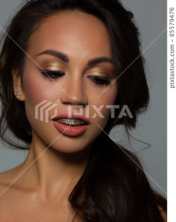 Close-up of woman's lips with fashion bright pink make-up and braces. Beautiful female mouth, full lips with perfect makeup. Part of female face. Choice lipstick. Brunet wavy hair of a Barbie doll Close-up of woman's lips with fashion bright pink make-up and braces. Beautiful female mouth, full lips with perfect makeup. Part of female face. Choice lipstick. Brunet wavy hair of a Barbie doll 85579476