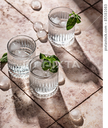 Cocktails with soda and mint leaves on a background of pink tiles with hard shadows Cocktails with soda and mint leaves on a background of pink tiles with hard shadows 85581083