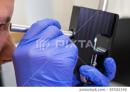 Scientist checking the condition of nebulizer needle from LC MS qTOF system using adjustment fixture and magnifier.  85582340