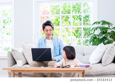 A kid sitting on the couch and working on a laptop talking to a dad at school 85583413