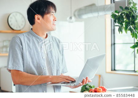 A man using a computer in front of the kitchen (smiles) 85583448