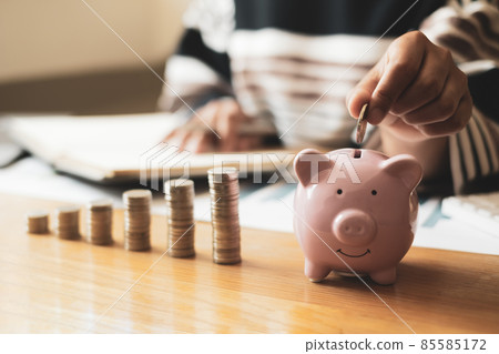 Woman's hand. putting coins in the piggy bank with coins, saving money with coins, stepping into a successful growing business, and saving for thought in retirement. Retirement savings concept Woman's hand. putting coins in the piggy bank with coins, saving money with coins, stepping into a successful growing business, and saving for thought in retirement. Retirement savings concept 85585172