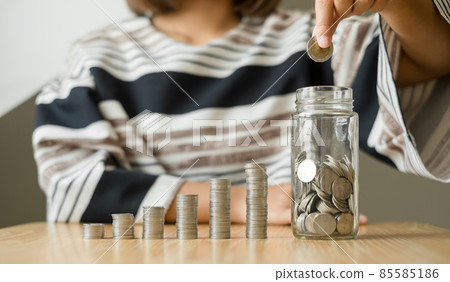 Woman's hand. Put a coin into a glass bottle with coins, saving money with coins, stepping into a successful growing business, and saving for thought in retirement. Retirement savings concept 85585186