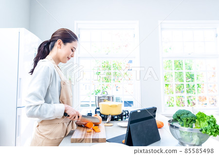 Housewife cooking while watching a video on a tablet in the kitchen Housewife cooking while watching a video on a tablet in the kitchen 85585498