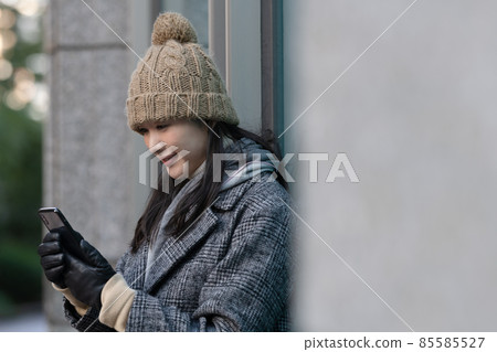 A woman leaning against a wall and operating a smartphone A woman leaning against a wall and operating a smartphone 85585527