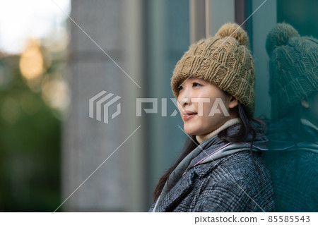 A woman leaning against the wall of a building and looking into the distance 85585543