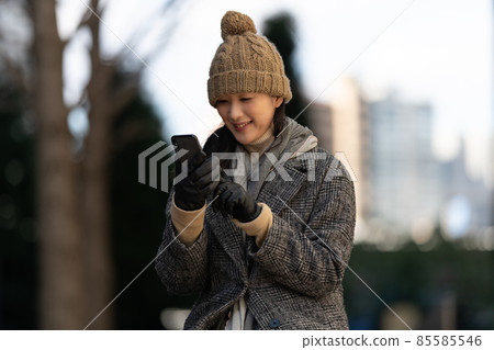 A woman sitting on an outdoor bench at dusk and operating a smartphone 85585546
