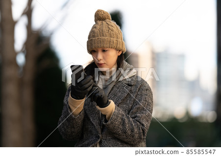 A woman sitting on an outdoor bench at dusk and operating a smartphone 85585547