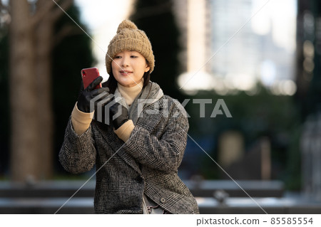A woman sitting on an outdoor bench at dusk and taking a selfie with her smartphone A woman sitting on an outdoor bench at dusk and taking a selfie with her smartphone 85585554