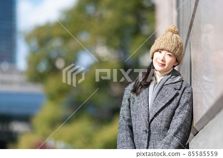 A woman standing leaning against the wall of a building A woman standing leaning against the wall of a building 85585559