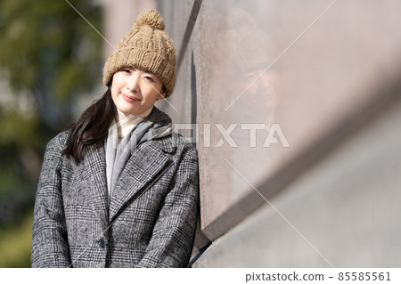 A woman standing leaning against the wall of a building A woman standing leaning against the wall of a building 85585561