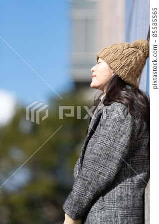 A woman standing leaning against the wall of a building A woman standing leaning against the wall of a building 85585565