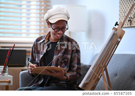 Smiling asian man painting picture with water color on easel. Smiling asian man painting picture with water color on easel. 85587105