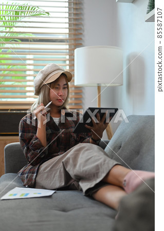 Asian woman sitting on sofa and working with digital tablet. Asian woman sitting on sofa and working with digital tablet. 85587107
