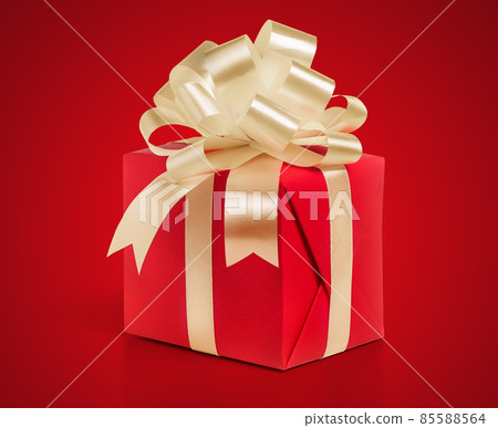 Gift box wrapped in a red paper with gold bow on a red background. 85588564