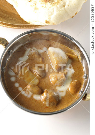 A bird's-eye view of hot massaman curry and naan containing many ingredients such as chicken and peanuts on a white background 85589657