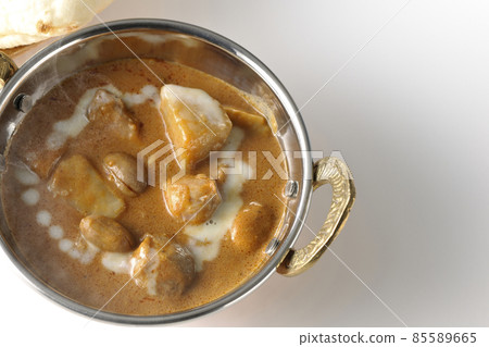 A bird's-eye view of hot massaman curry and naan containing many ingredients such as chicken and peanuts on a white background 85589665
