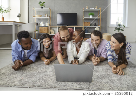 Diverse group of happy young multiracial college students and friends having friendly gathering at home, lying together on floor in living room, watching funny movie or TV show on laptop and laughing Diverse group of happy young multiracial college students and friends having friendly gathering at home, lying together on floor in living room, watching funny movie or TV show on laptop and laughing 85590012