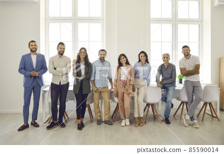 Group portrait of happy multi aged business people at work. Team of successful young and mature company employees in smart casual clothes standing together by a table in a modern bright office Group portrait of happy multi aged business people at work. Team of successful young and mature company employees in smart casual clothes standing together by a table in a modern bright office 85590014