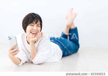 一位年輕女子躺在客廳裡,看著她的智能手機 一位年輕女子躺在客廳裡,看著她的智能手機 85593015