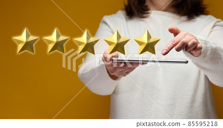 female hand holding an electronic gadget tablet on a yellow background, five gold stars 85595218