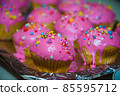 Freshly baked vanilla muffins are garnished with sweet icing and topping. 85595712