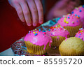 Freshly baked vanilla muffins are garnished with sweet icing and topping. 85595720