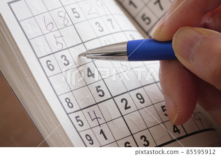 Hands of a person who is doing Sudoku with a ballpoint pen 85595912