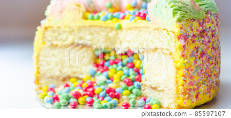 Madeira sponge coated with yellow colour frosting, layered with plum and raspberry jam, filled and topped with multicolour chocolate nibs and decorated with multicolour frostings and sugar decorations 85597107