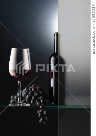 Bottle and a glass of red wine with a bunch of blue grapes. Bottle and a glass of red wine with a bunch of blue grapes. 85597337