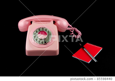 Vintage Pink Telephone with Pen and Notebook on a Black Background 85598440