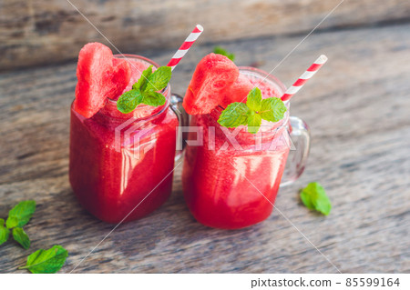 Healthy watermelon smoothie in Mason jars with mint and striped straws on a wood background Healthy watermelon smoothie in Mason jars with mint and striped straws on a wood background 85599164