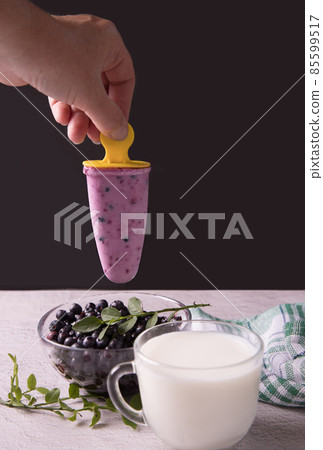 A woman's hand holds homemade ice cream with berries over a plate of blueberries. The concept of natural products 85599517