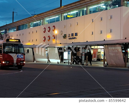 A two-story station building. There is a bus rotary in front of the station 85599642