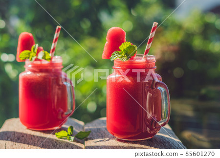 Healthy watermelon smoothie in Mason jars with mint and striped straws against the background of greenery 85601270