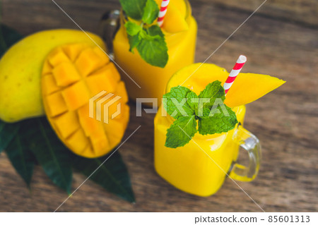 Juicy smoothie from mango in two glass mason jars with striped red straw on old wooden background. Healthy life concept, copy space Juicy smoothie from mango in two glass mason jars with striped red straw on old wooden background. Healthy life concept, copy space 85601313