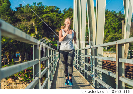 Beautiful woman running over bridge during sunset Beautiful woman running over bridge during sunset 85601316