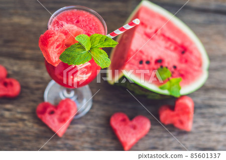 Healthy watermelon smoothie with mint, a piece of watermelon, hearts and a striped straw on a wood background Healthy watermelon smoothie with mint, a piece of watermelon, hearts and a striped straw on a wood background 85601337
