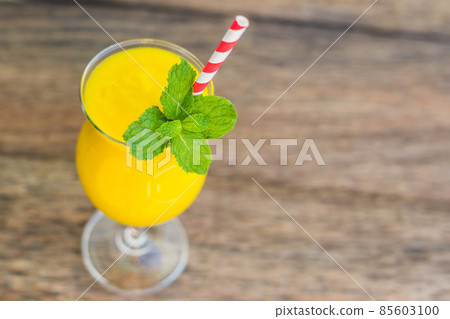 Juicy smoothie from mango in glass with striped red straw and with a mint leaf on old wooden background. Healthy life concept, copy space Juicy smoothie from mango in glass with striped red straw and with a mint leaf on old wooden background. Healthy life concept, copy space 85603100