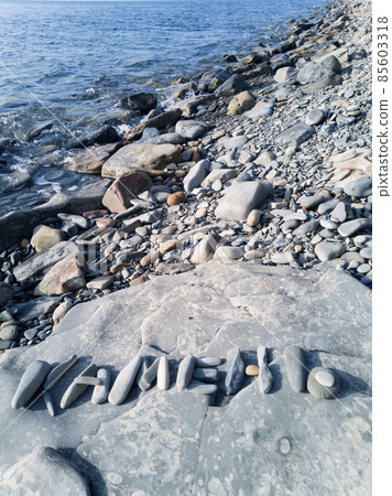 On a large stone on the seashore, the inscription "Stone" is laid out in Russian letters On a large stone on the seashore, the inscription "Stone" is laid out in Russian letters 85603318