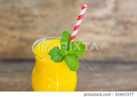 Juicy smoothie from mango in glass with striped red straw and with a mint leaf on old wooden background. Healthy life concept, copy space 85603377