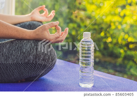 hand of a woman meditating in a yoga pose on a rug for yoga and a bottle of water 85603405